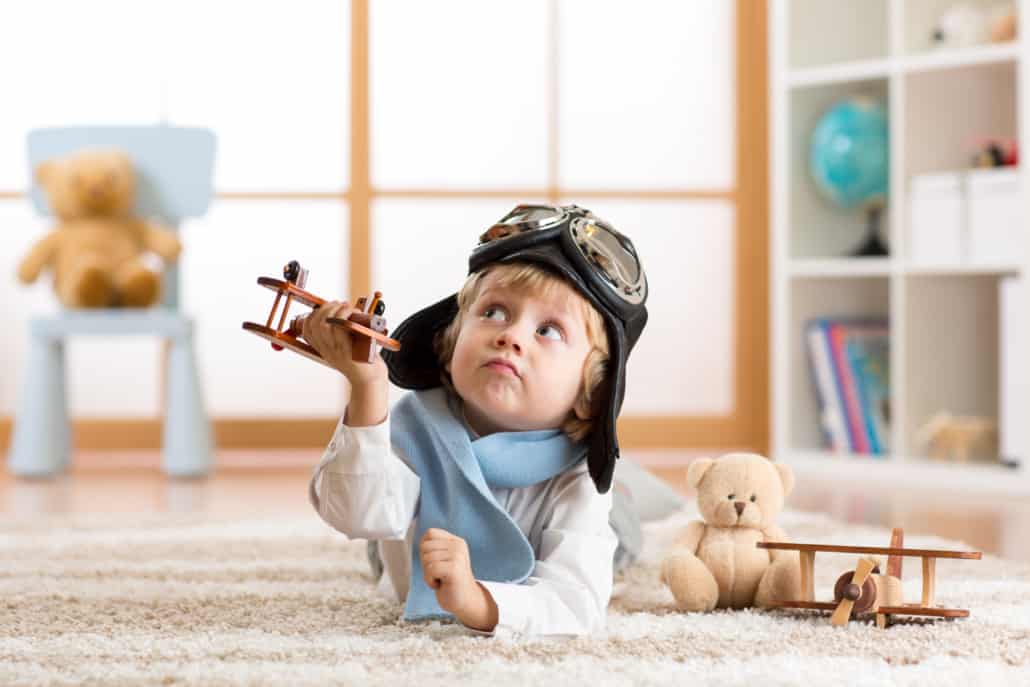 kid holding a airplane wooden toy laying on a carpet and looking up